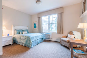 Bedroom with queen-sized bed, armchair, dresser and nightstand in senior living apartment