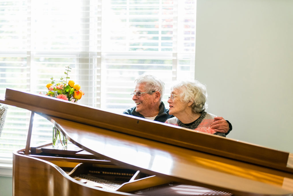 Older couple sitting behind the open lid of a grand piano