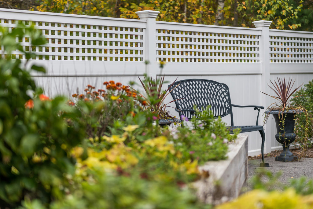 Patio chair in front of a fence alongside a flower garden