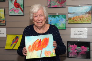 Eleanor McCarthy displays her painting of tulips as she stands before all of her entries at the art show. A detailed view of her blossoms in reflection can be seen below.