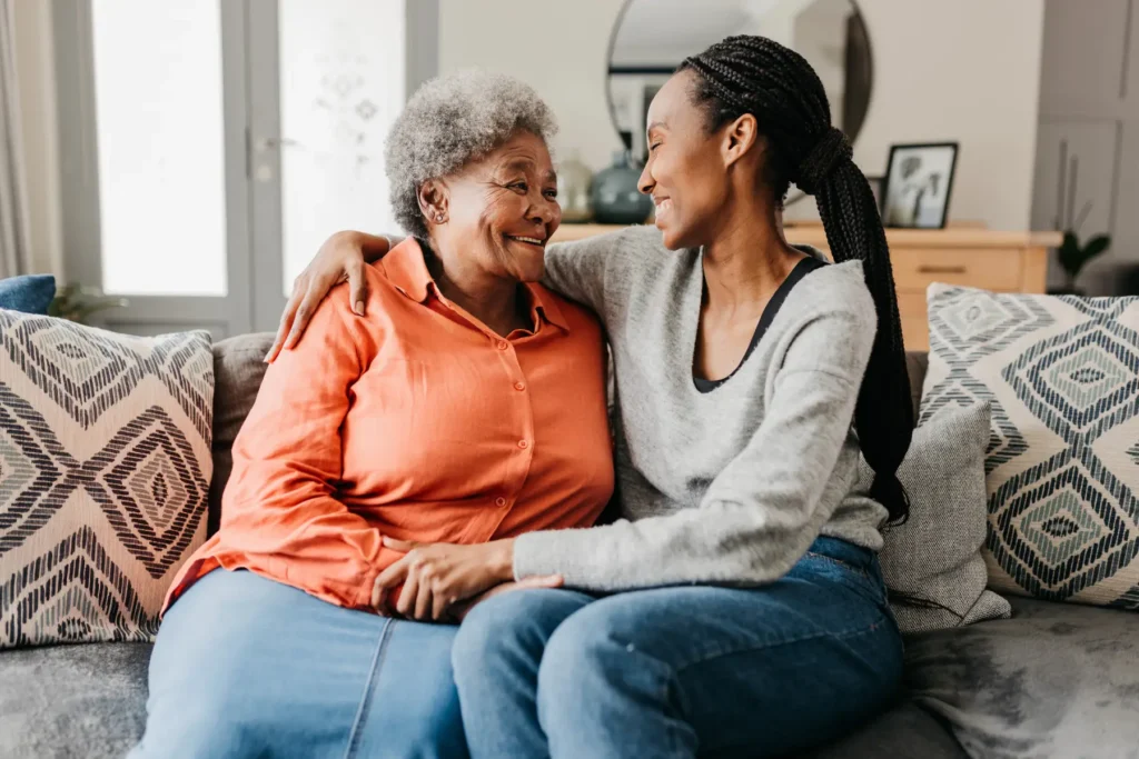 a woman sitting on the couch with her arm around her senior mother
