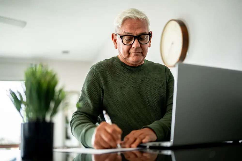 a senior man taking notes while in front of his computer