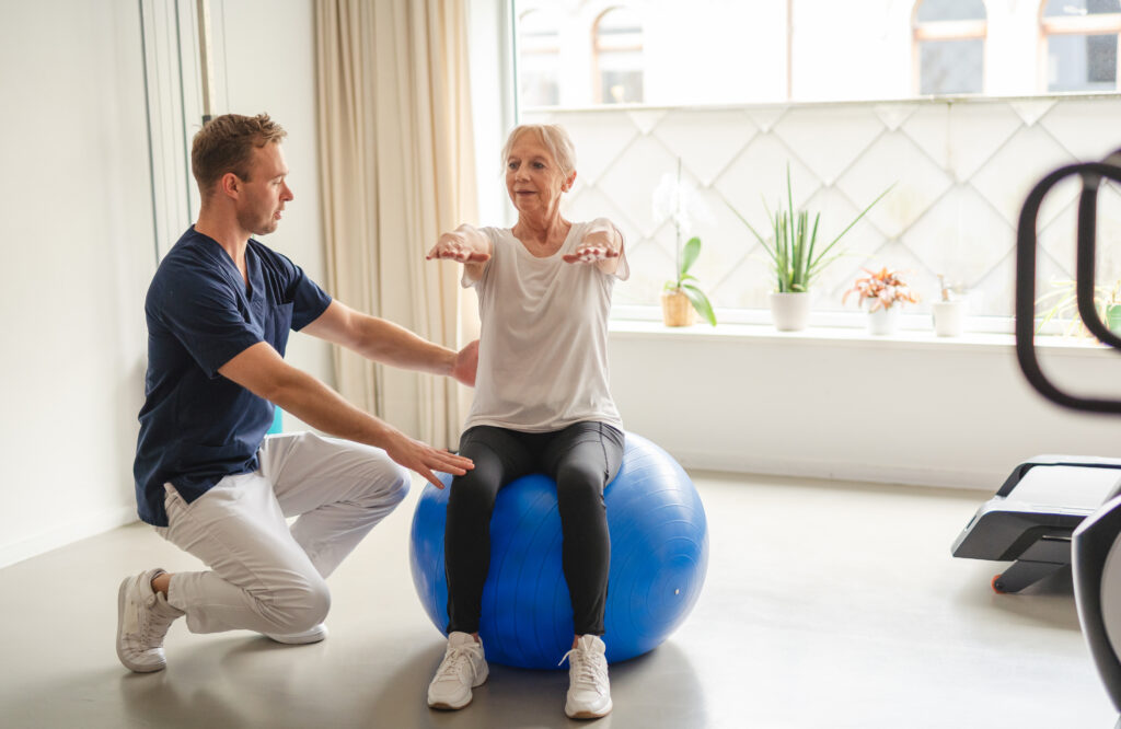 A young physiotherapist guiding an elderly woman through senior rehabilitation exercises on exercise ball